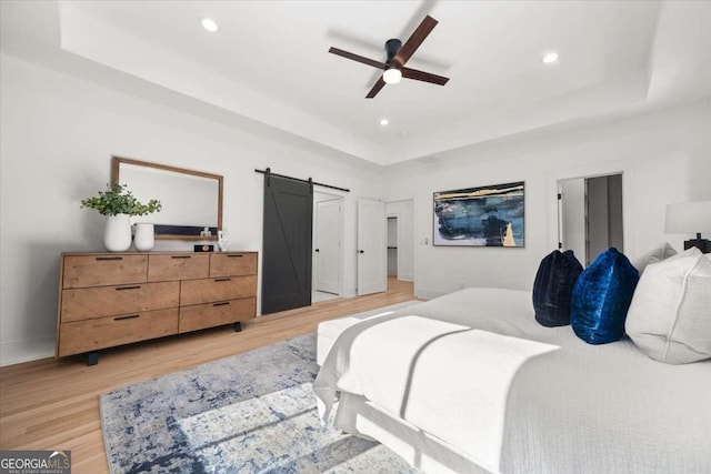 bedroom with recessed lighting, light wood-style floors, a tray ceiling, and a barn door
