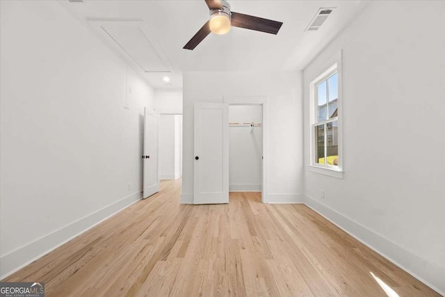 unfurnished bedroom featuring attic access, baseboards, visible vents, a walk in closet, and light wood-type flooring