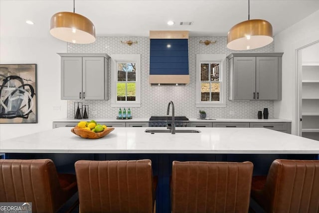 kitchen featuring light countertops, a sink, gray cabinets, wall chimney range hood, and decorative backsplash