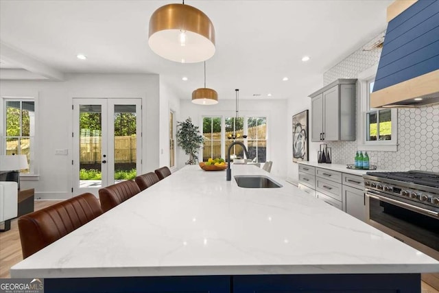 kitchen with a sink, high end stainless steel range oven, backsplash, a large island, and custom exhaust hood