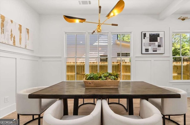 dining room with a decorative wall, a notable chandelier, light wood-type flooring, and visible vents