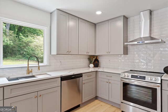 kitchen with a sink, tasteful backsplash, wall chimney range hood, appliances with stainless steel finishes, and gray cabinetry