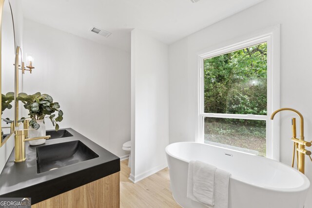 full bathroom featuring toilet, baseboards, visible vents, a soaking tub, and wood finished floors