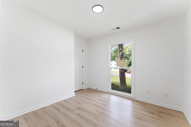 empty room with light wood finished floors, visible vents, and baseboards