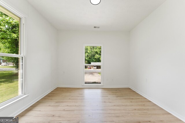 spare room featuring light wood finished floors, baseboards, a healthy amount of sunlight, and visible vents