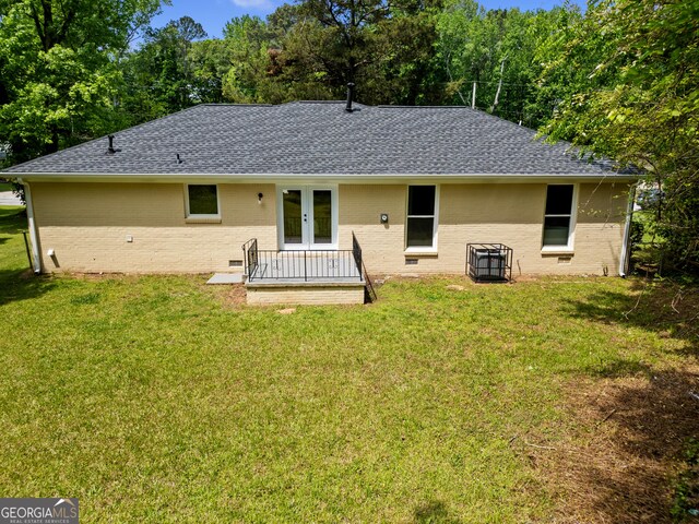 rear view of property featuring a yard, roof with shingles, french doors, and brick siding
