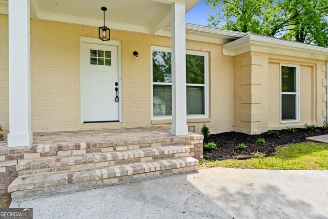 doorway to property with a porch and brick siding
