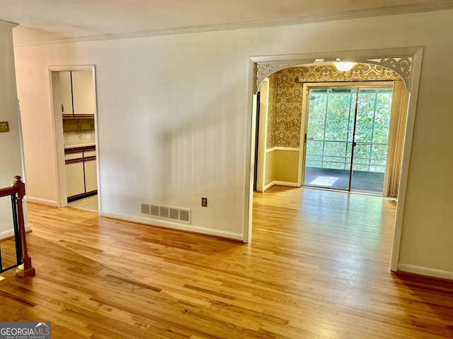spare room featuring light wood finished floors, ornamental molding, baseboards, and visible vents