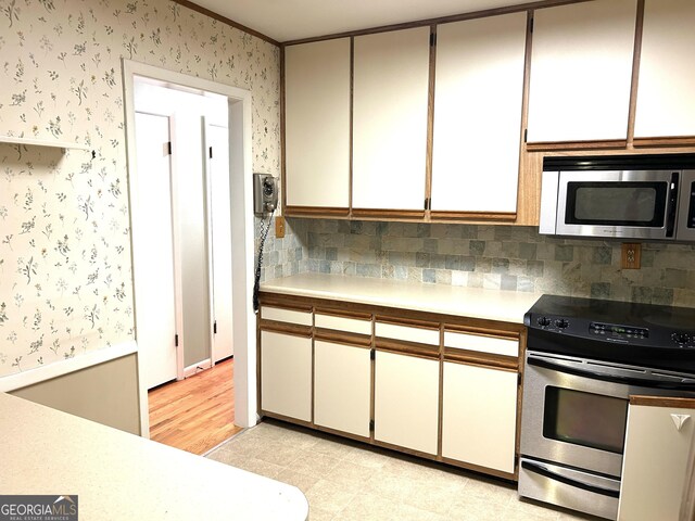 kitchen with light countertops, appliances with stainless steel finishes, decorative backsplash, and wallpapered walls