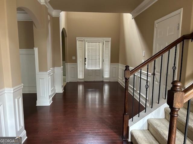 entrance foyer featuring stairway, a decorative wall, wainscoting, arched walkways, and hardwood / wood-style flooring