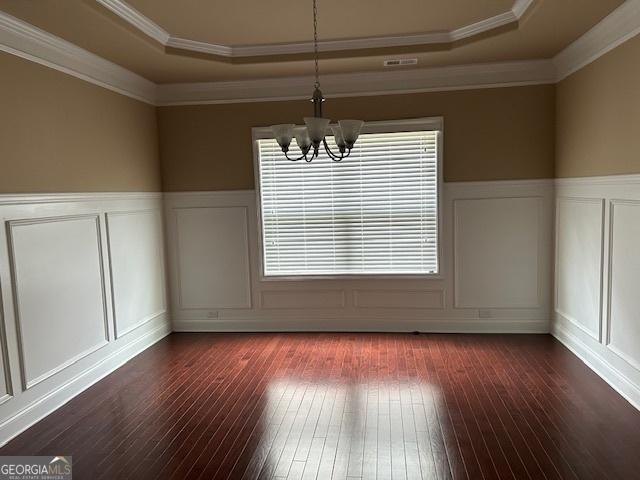 unfurnished dining area featuring a tray ceiling, a chandelier, wood-type flooring, and a decorative wall