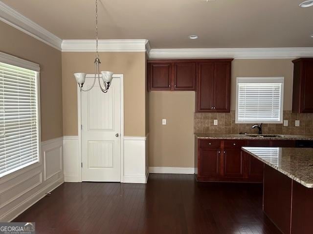 kitchen with light stone countertops, dark wood-style flooring, an inviting chandelier, a sink, and crown molding