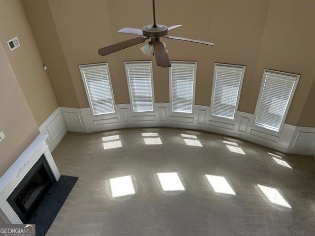unfurnished living room with a ceiling fan, carpet, a decorative wall, a wainscoted wall, and a towering ceiling