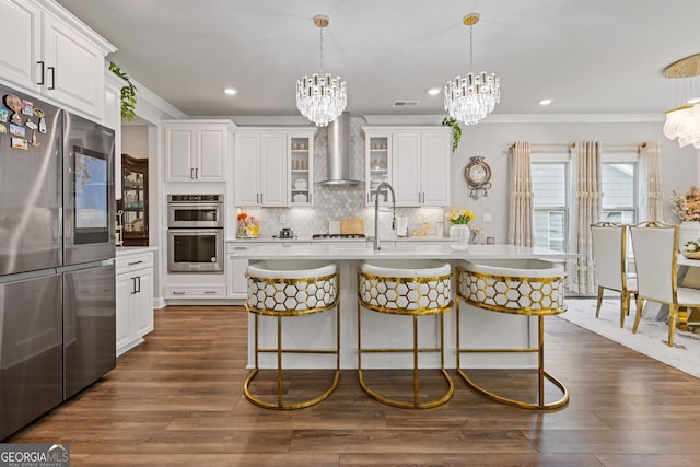 kitchen with wall chimney exhaust hood, a notable chandelier, crown molding, light countertops, and appliances with stainless steel finishes