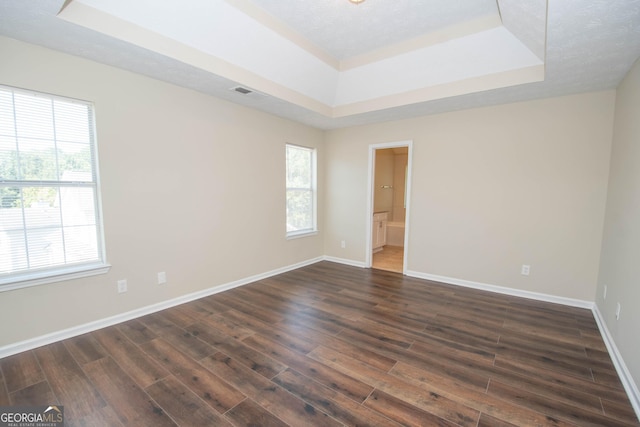 spare room with a raised ceiling, a wealth of natural light, dark wood-type flooring, and visible vents