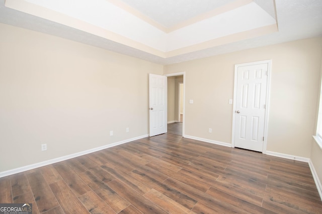 spare room with a tray ceiling, dark wood-type flooring, and baseboards