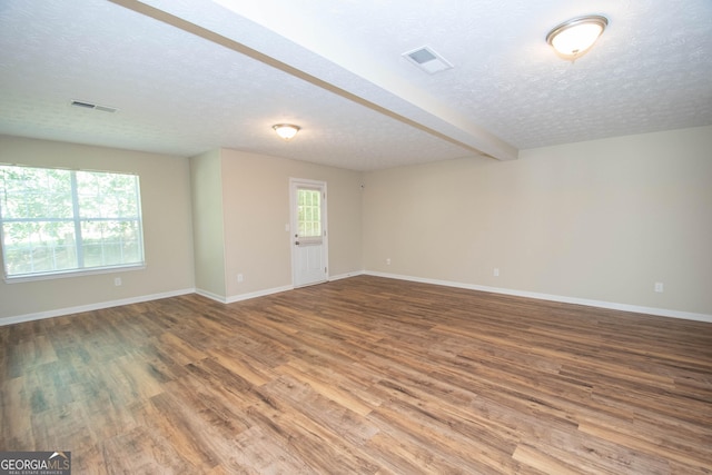 unfurnished room featuring baseboards, visible vents, a textured ceiling, and wood finished floors