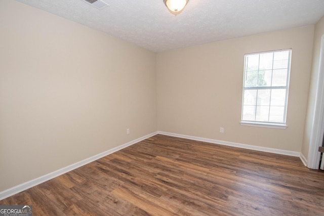 spare room with a textured ceiling, dark wood-type flooring, baseboards, and visible vents