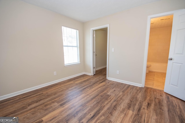 unfurnished bedroom with ensuite bathroom, wood finished floors, and baseboards