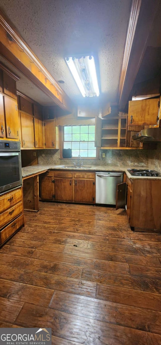 kitchen with a sink, stainless steel appliances, brown cabinets, a textured ceiling, and dark wood finished floors