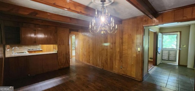 unfurnished dining area with a sink, beam ceiling, wooden walls, dark wood-style floors, and a notable chandelier