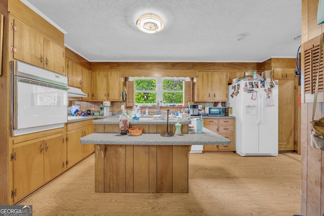kitchen with a center island, a textured ceiling, white appliances, light countertops, and light wood-style floors