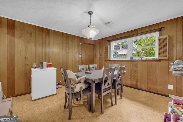 dining room featuring wooden walls, visible vents, a textured ceiling, and light wood-style floors