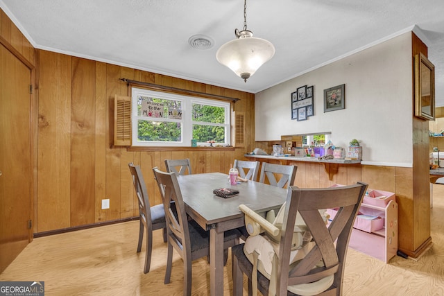dining space with wooden walls, light wood finished floors, crown molding, and visible vents