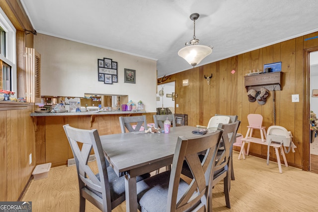 dining room with ornamental molding, wood walls, and light wood-type flooring