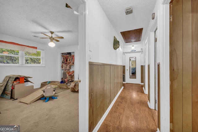 hallway with a textured ceiling, attic access, and wood finished floors