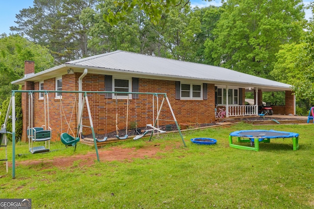back of house with a chimney, a lawn, brick siding, metal roof, and a trampoline