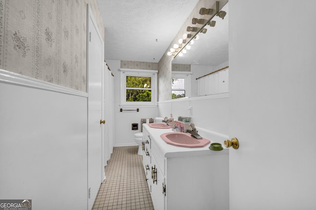 bathroom with toilet, a textured ceiling, double vanity, and a sink
