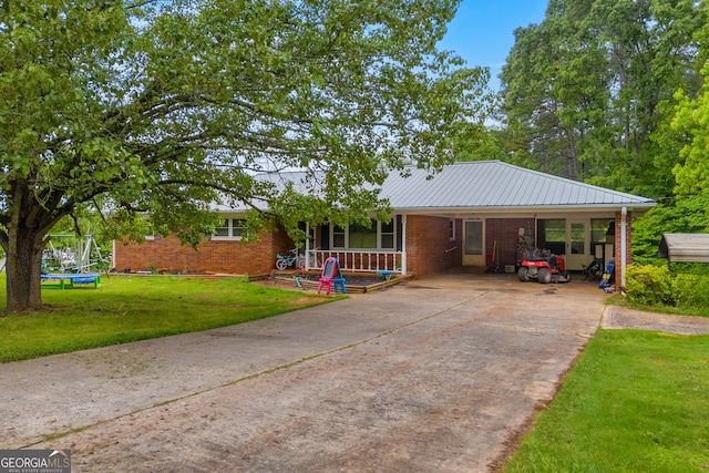 ranch-style house featuring an attached carport, a trampoline, a front lawn, brick siding, and driveway