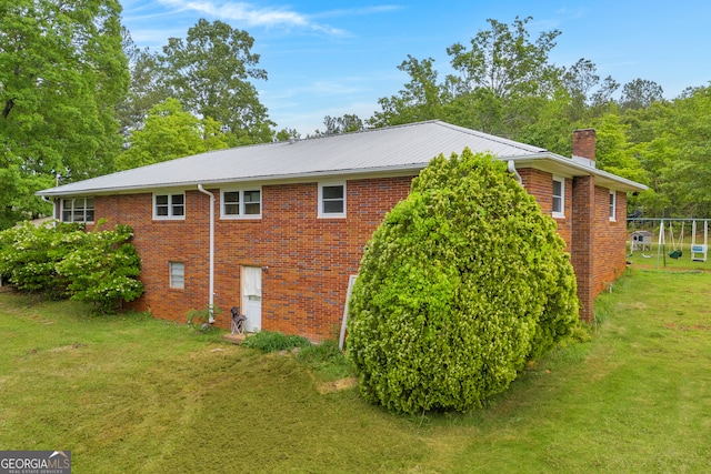 view of home's exterior featuring brick siding, metal roof, a chimney, and a lawn