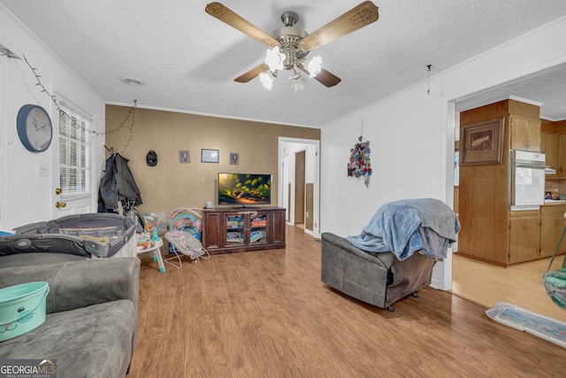 living area featuring a ceiling fan, light wood-style floors, crown molding, and a textured ceiling