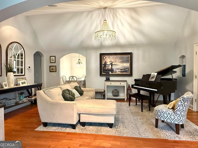 living room with arched walkways, a chandelier, vaulted ceiling, and wood finished floors