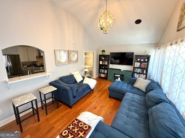 living room with a chandelier, arched walkways, high vaulted ceiling, and wood finished floors