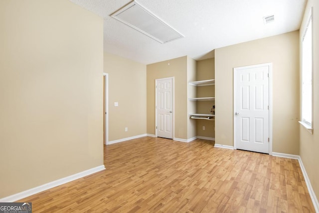 unfurnished bedroom with light wood finished floors, attic access, baseboards, and visible vents