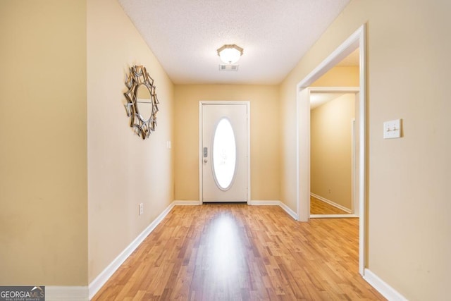 foyer entrance featuring light wood-type flooring, visible vents, baseboards, and a textured ceiling