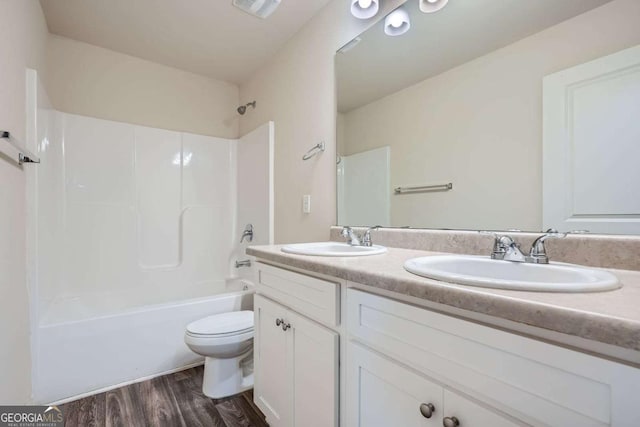 full bath with toilet, double vanity, a sink, and wood finished floors