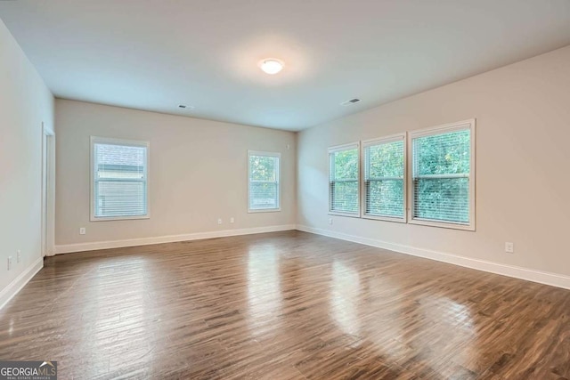 unfurnished room with visible vents, baseboards, and dark wood-style floors