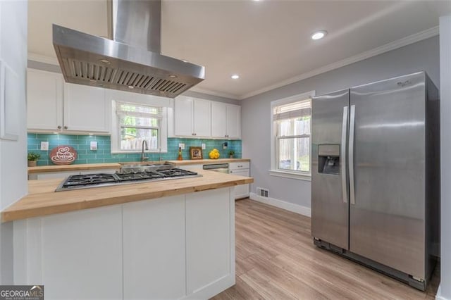 kitchen featuring stainless steel appliances, wall chimney range hood, crown molding, white cabinetry, and wooden counters