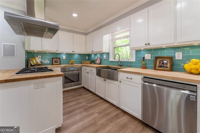 kitchen with butcher block counters, a sink, ventilation hood, stainless steel appliances, and white cabinets