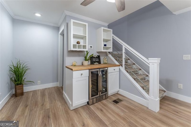 bar with a bar, crown molding, light wood-type flooring, wine cooler, and stairs