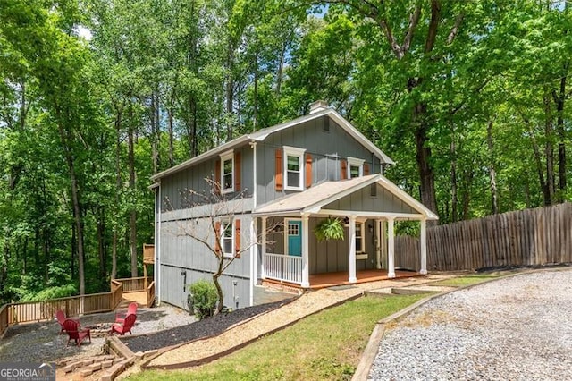 view of front facade with an outdoor fire pit, a porch, a chimney, and fence