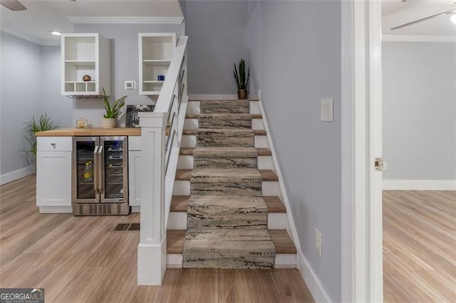 stairway featuring beverage cooler, wood finished floors, ceiling fan, and crown molding