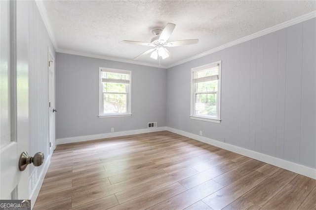 spare room with light wood finished floors, crown molding, plenty of natural light, and visible vents