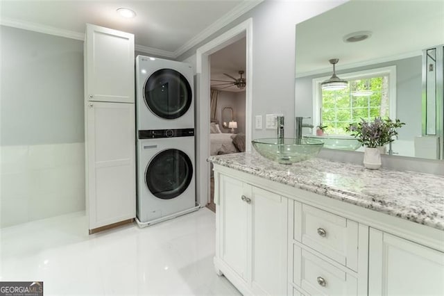 washroom with a ceiling fan, stacked washer / dryer, ornamental molding, a sink, and laundry area