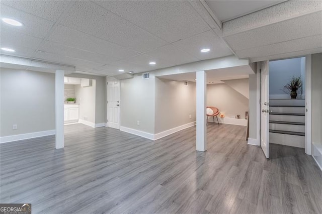 finished below grade area with a drop ceiling, wood finished floors, visible vents, baseboards, and stairs