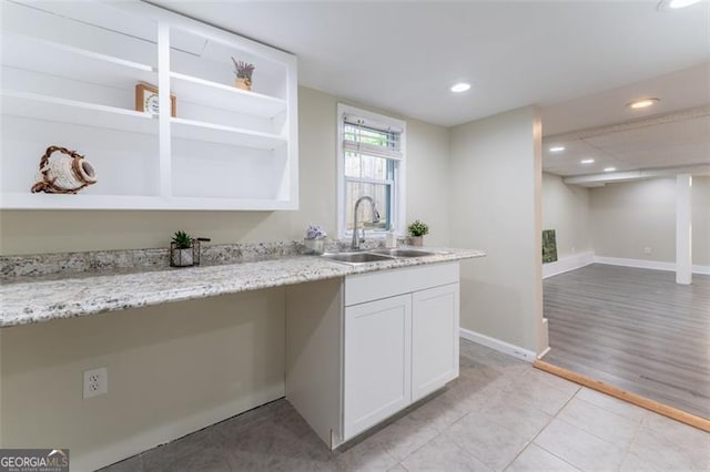 kitchen featuring a sink, light stone counters, recessed lighting, white cabinets, and baseboards
